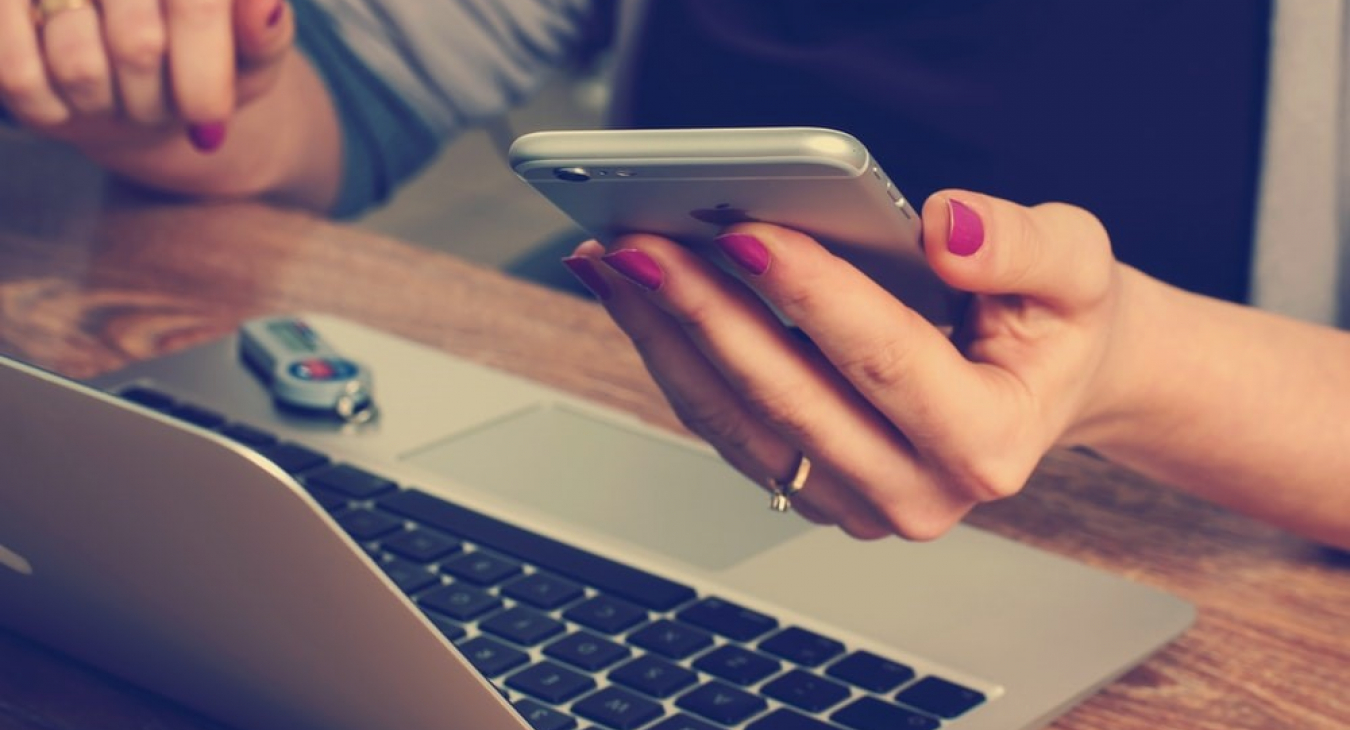 image of person behind a laptop with smartphone in her hands